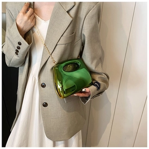 Detail of metallic green acrylic handbag with gold chain strap on beige blazer