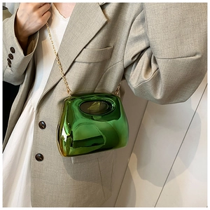 Detail of metallic green acrylic handbag with gold chain strap worn by a model