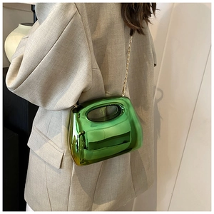 Detail shot of bright green acrylic handbag with gold chain strap on model outfit