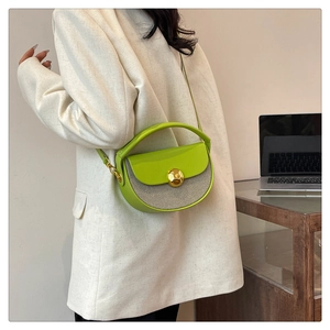 Detailed side view of a green leather saddle bag with a golden metal ball clasp worn by a model