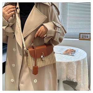Dettaglio della borsa in paglia intrecciata con patta in pelle marrone e ciondolo a fiore