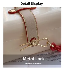 Detail of elegant gold hardware clasp on creamy white acrylic handbag with red trim