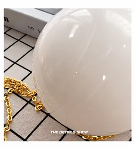Detail view of smooth white pearl sphere and thick gold chain strap on stylish round bag