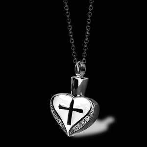 Dettaglio del ciondolo a cuore per ceneri con croce nera e cristalli su sfondo nero