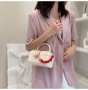 Modern white acrylic box handbag with bold red chain detail on model in pink suit