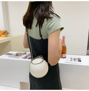 Close-up of white spherical hard shell bag with gold ring handle and chain strap