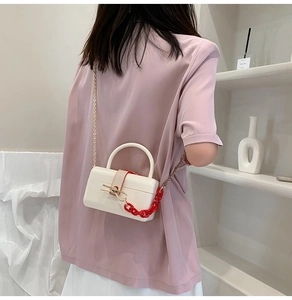 Detail view of white glossy acrylic box bag with red chain and gold shoulder strap