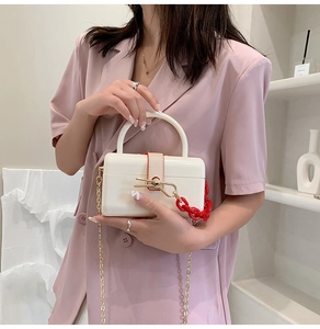 Detail of a creamy white acrylic vanity box bag with red resin chain held by a model