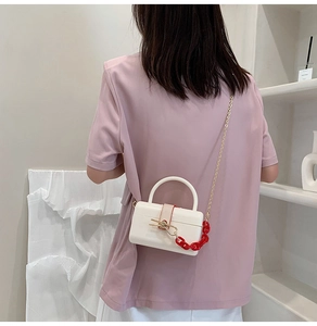 Close-up of a white acrylic box bag with red chunky chain and golden shoulder strap