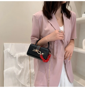 Detail of black box bag with bold red acrylic chain and golden metallic hardware buckle