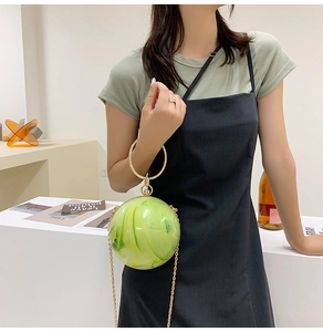Model holding a spherical marble green acrylic clutch bag with a gold ring handle