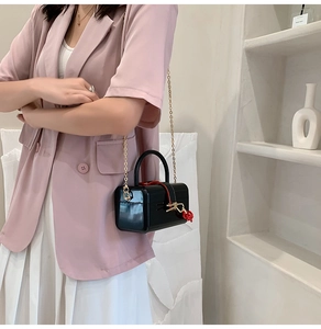 Detail of black glossy box bag with gold chain strap and red knot charm on a model
