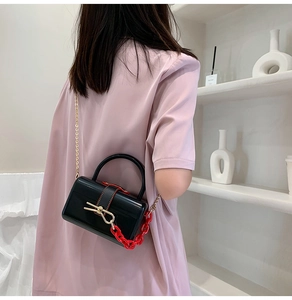 Detail of black acrylic box bag featuring red chunky chain and gold metal strap
