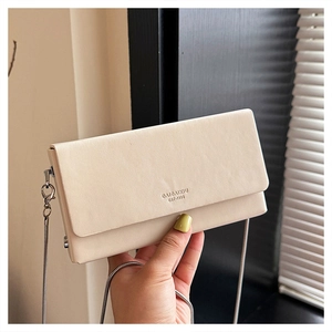 Close-up of cream square chain bag with silver strap and brand logo on leather