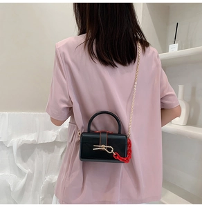 Detail of a black hard-shell box bag with gold and red chain straps on a model