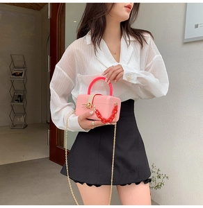 Pink mini square bag with red top handle and metal chain shown on model in modern setting