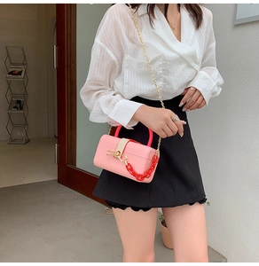 Detail of pink structured bag featuring a bold red accent chain and gold shoulder strap