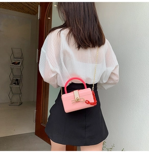 Detail of pink box bag with red resin handle and gold chain strap worn by a model