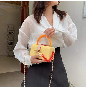 Yellow acrylic box bag with orange handle and red chain shown on a female model