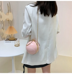 Pink spherical crossbody bag with gold chain strap worn over a white blazer