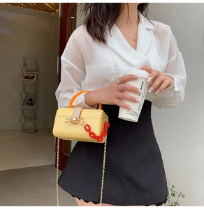 Street style shot of a yellow acrylic box bag with orange handle and chunky red chain