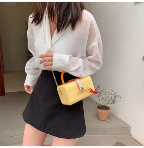 Detail of yellow box handbag with orange handle and gold chain strap in a modern setting