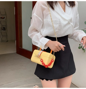 Detail of yellow box bag with red acrylic chain and orange handle on a fashion model