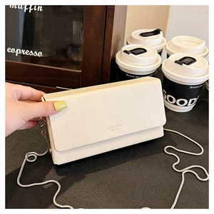 Close-up of minimalist cream leather crossbody bag with silver chain in a cafe setting