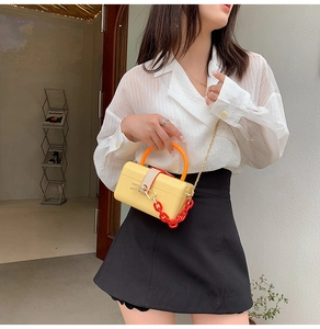 Detailed view of yellow box bag featuring orange handle and red decorative chain strap