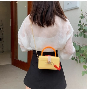 Fashionable bright yellow acrylic box bag with orange handle and red chain crossbody detail