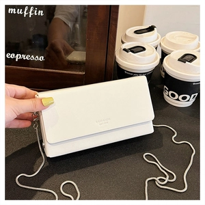 Detailed shot of white rectangular chain bag with gold snake strap on a cafe table