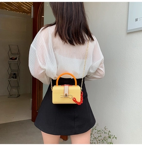 Detailed view of yellow mini box bag with orange handle and red acrylic chain on model