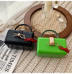 Chic acrylic box handbags in black and green with red chain detail on a cozy blanket