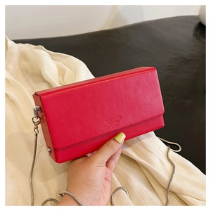 Detail of red leather crossbody bag featuring silver chain strap and embossed logo