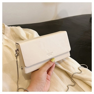 Close-up of white matte leather crossbody bag with silver chain and embossed logo detail