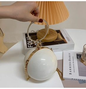Detail of white spherical evening clutch bag with rhinestone ring handle and gold chain