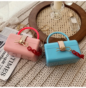 Detailed shot of pastel acrylic box bags with gold chains and bow clasps on a cozy background