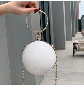 Detailed view of a white spherical evening bag with a rhinestone-studded gold ring handle