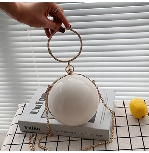 Detail of a white spherical evening bag with pearl finish and rhinestone metal handle