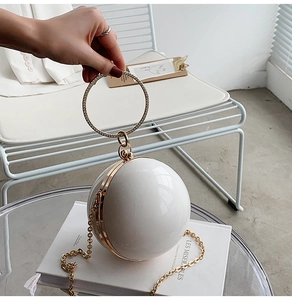 Close-up of a white sphere clutch bag featuring a gold rhinestone-encrusted ring handle
