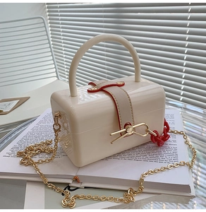 Detail of cream acrylic box bag with golden chain and red-edged leather buckle