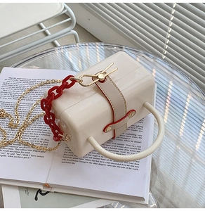Close-up of creamy white acrylic box bag with decorative red chain and gold shoulder strap