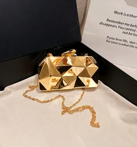 Detail of a geometric gold cube clutch bag with mirror finish and delicate chain strap