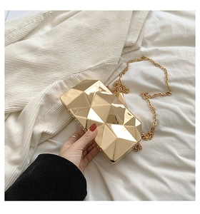 Macro detail of golden geometric cube evening clutch with metallic chain strap
