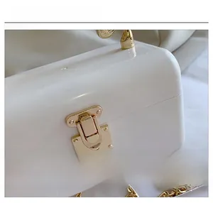 Detail shot of the golden metal hinge and chain strap on a white acrylic evening bag