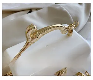 Detail showing the elegant gold leopard-shaped handle on a white acrylic clutch bag