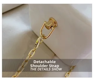 Detail of detachable gold metal chain strap on white acrylic clutch bag showing D-ring