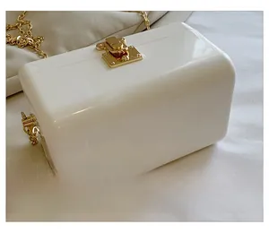 Detail of a white acrylic box handbag featuring a gold square metal lock and chain