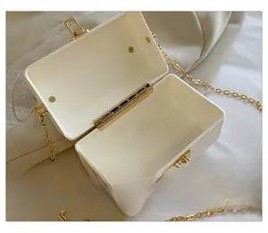 Detail showing the square white acrylic clutch bag with golden chain strap and inner compartments