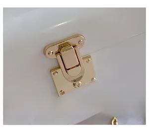 Close-up of premium gold metal clasp and chain on white acrylic evening clutch bag
